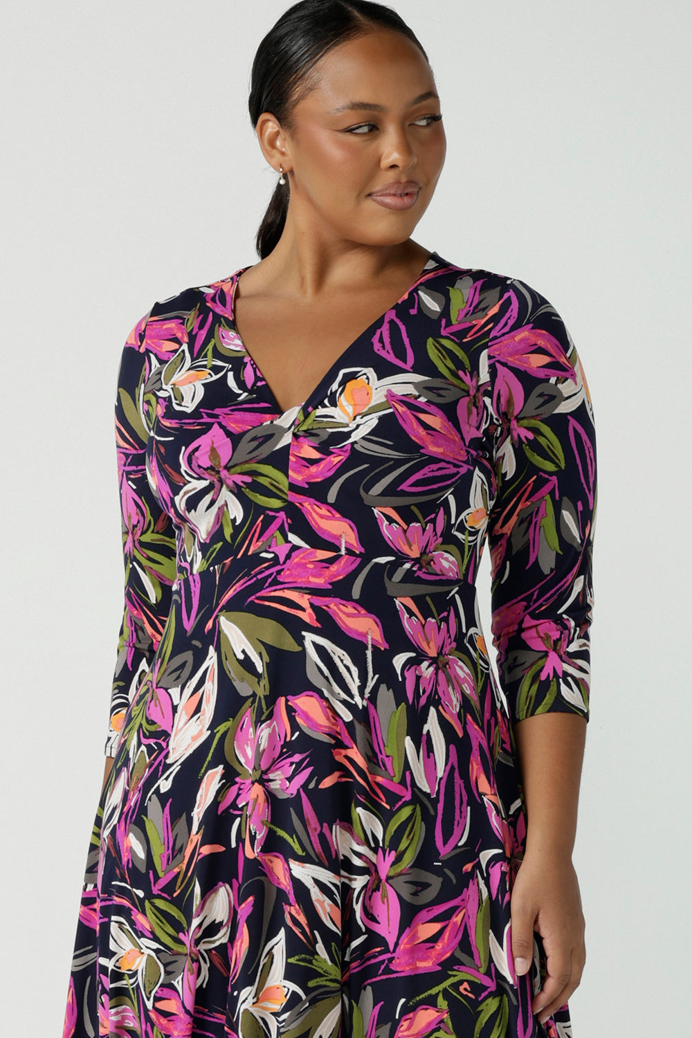 Close up of a size 16 woman wears a Kyra dress in Vivid Flora. Empire line fit and flare style with a 3/4 sleeve. Twist front neckline. Flattering shape for all sizes 8 - 24. Made in Australia for corporate casual women.