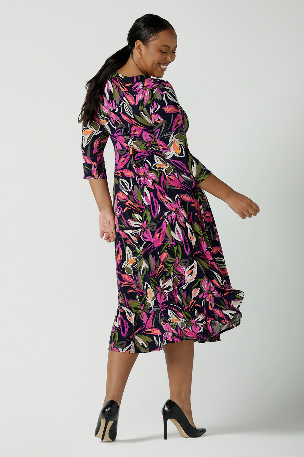 Back view of a size 16 woman wears a Kyra dress in Vivid Flora. Empire line fit and flare style with a 3/4 sleeve. Twist front neckline. Flattering shape for all sizes 8 - 24. Made in Australia for corporate casual women.