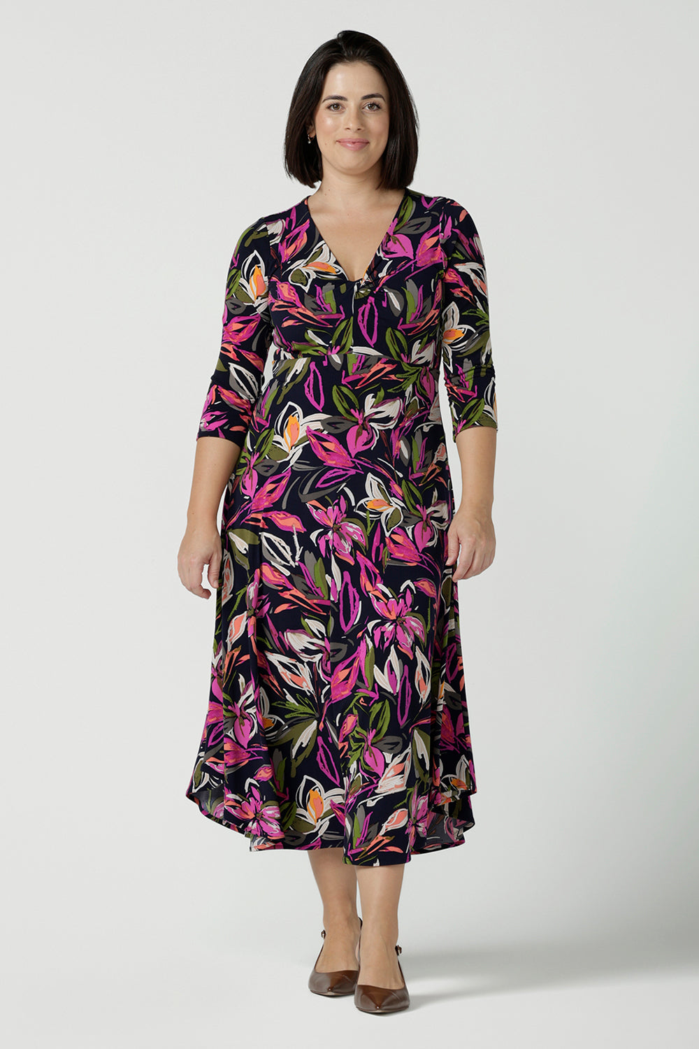 A size 10 woman wears a Kyra dress in Vivid Flora. Empire line fit and flare style with a 3/4 sleeve. Twist front neckline. Flattering shape for all sizes 8 - 24. Made in Australia for corporate casual women.
