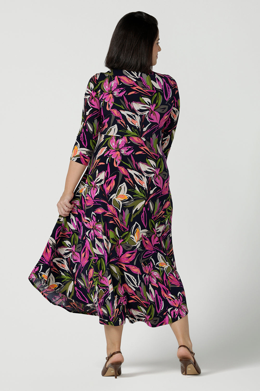 Back view of a size 10 woman wears a Kyra dress in Vivid Flora. Empire line fit and flare style with a 3/4 sleeve. Twist front neckline. Flattering shape for all sizes 8 - 24. Made in Australia for corporate casual women.