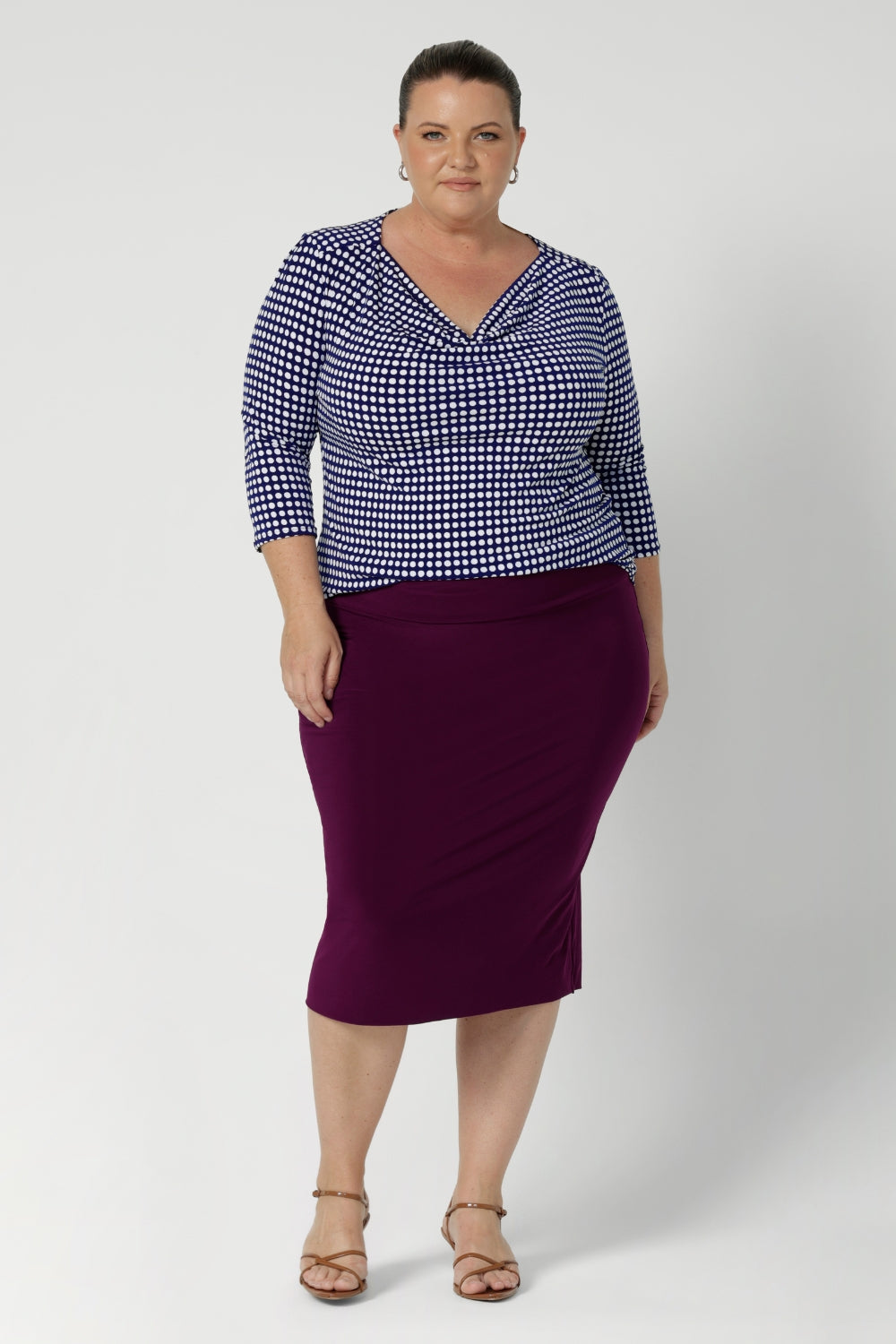 Plus size woman wears her Kyrie Top in Polka Dot untucked with a magenta coloured tube skirt and brown kitten heels.  This cowl neck top matches with many colours and is a versatile styling piece for the working woman. Available in sizes 8-24.