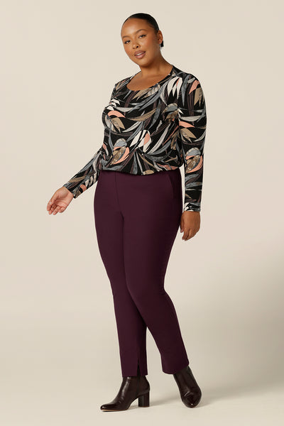A scoop neck, long sleeve jersey top in black based floral print is worn with slim leg, stretch pants in Mulberry red. Made in Australia by women's clothing label, Leina and Fleur, this women's work top is available to shop in sizes 8 to 24 and is a good plus size top for women with fuller figures. 