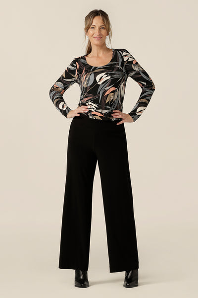 A scoop neck, long sleeve jersey top in black based floral print is worn with straight cut, wide leg black trousers for a comfortable yet elegant work outfit. Made in Australia by women's clothing label, Leina and Fleur, this women's work top is available to shop in sizes 8 to 24.
