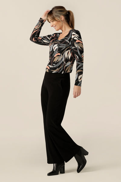 A scoop neck, long sleeve jersey top in black based floral print is worn with straight cut, wide leg black trousers for comfortable and elegant office style. Made in Australia by women's clothing label, Leina and Fleur, this women's work top is available to shop in sizes 8 to 24.