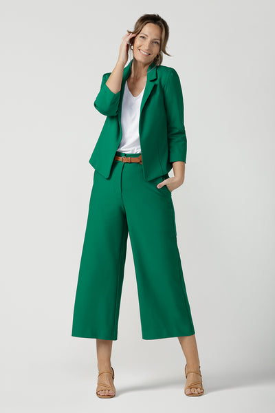 A size 10 woman wears a tailored jacket with open front and collar and notch lapels is made in Emerald green ponte fabric. Styled with wide-leg cropped Emerald green tailored pants for a fresh workwear look. Shop exclusive luxury, this work jacket is available at Australian and New Zealand women's clothing label, L&F.