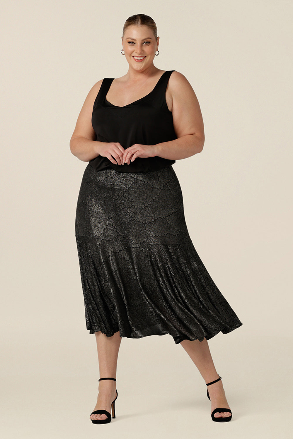 A size 18, plus size woman wears a midi length, foil print evening skirt with ruffle hem. For cocktail and evening wear, this elegant skirt is worn with a black cami top. Both going out skirt and top are made in Australia by women's fashion brand, Leina & Fleur. Shop their evening and cocktail wear online in sizes 8 to 24.