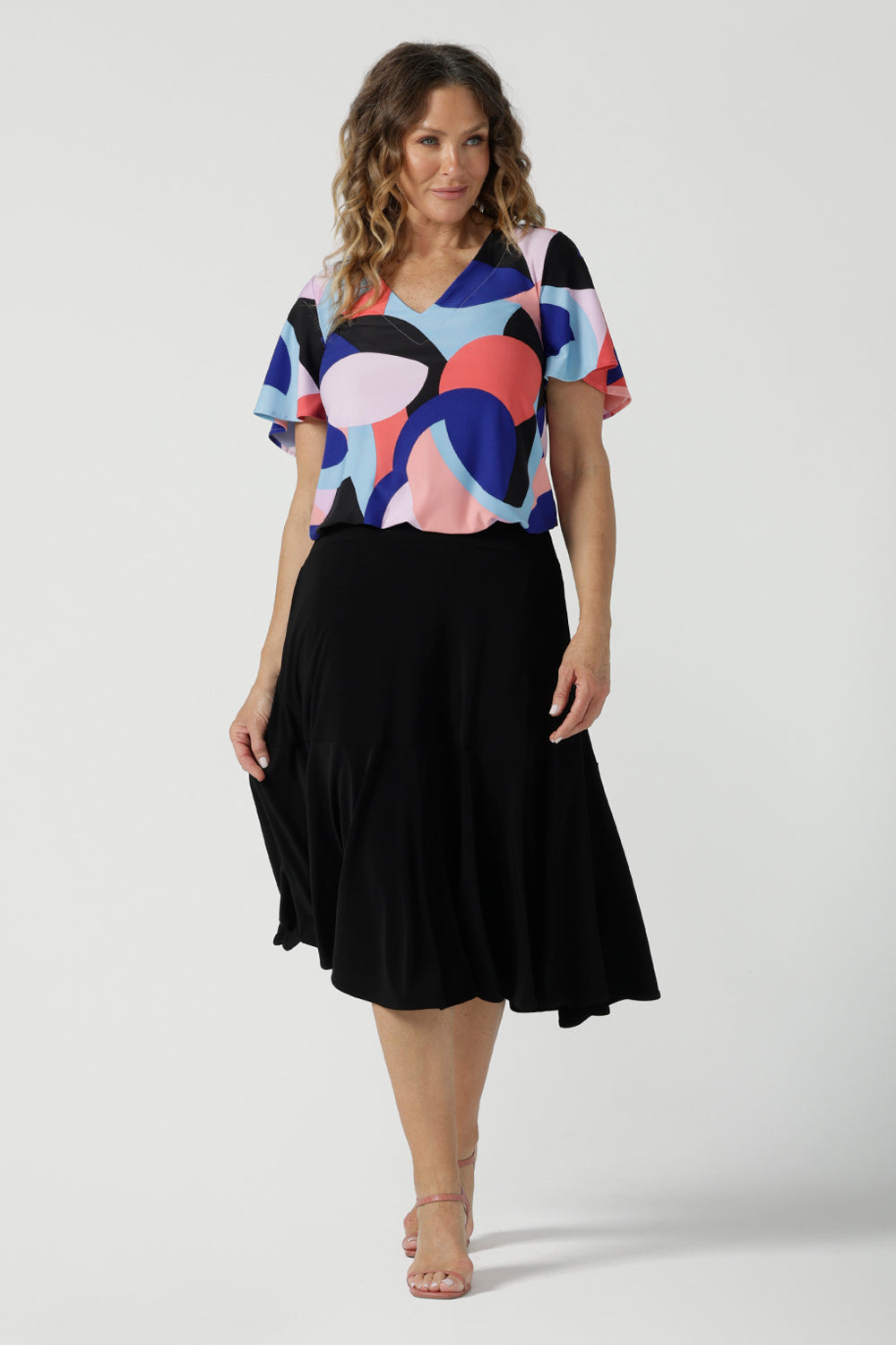 A size 10 woman wears the Lila Top in Amalfi. A jersey tpoo with flutter sleeves and an abstract print. Made in Australia for women size 8-24. Back with a Berit Black skirt. 