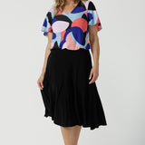 A size 10 woman wears the Lila Top in Amalfi. A jersey tpoo with flutter sleeves and an abstract print. Made in Australia for women size 8-24. Back with a Berit Black skirt. 