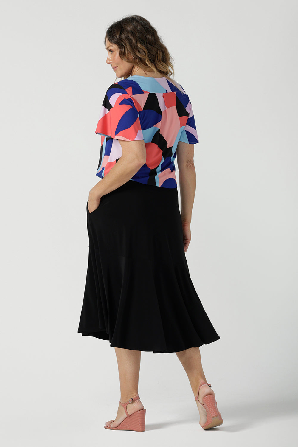 A size 10 woman wears the Lila Top in Amalfi. A jersey tpoo with flutter sleeves and an abstract print. Made in Australia for women size 8-24. Back with a Berit Black skirt. 