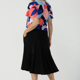 A size 10 woman wears the Lila Top in Amalfi. A jersey tpoo with flutter sleeves and an abstract print. Made in Australia for women size 8-24. Back with a Berit Black skirt. 