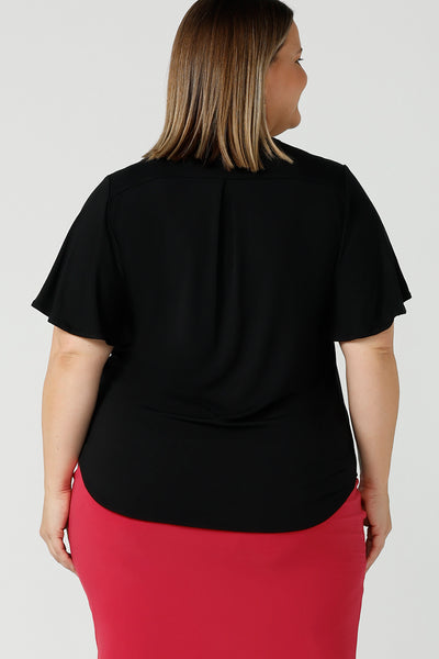 Back view of a flutter sleeve, black top for work and casual wear, this tailored top is worn by a size 18 curvy woman. Made in Australia, shop women's black tops online at Australian and New Zealand women's clothing brand, Leina & Fleur.