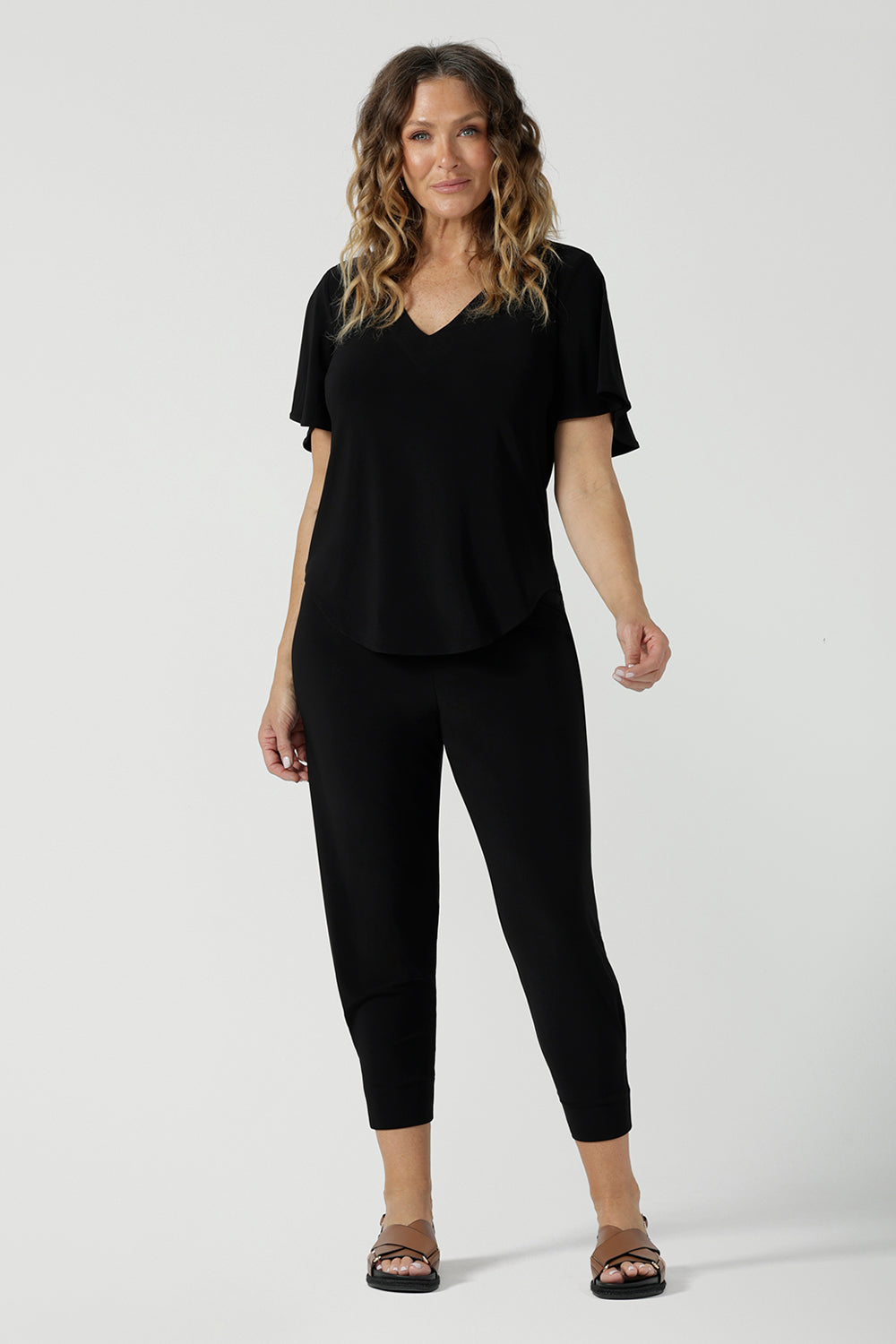 A size 10 woman wears the Lila Top in Black, a jersey workwear top for women for flutter sleeve and v-neckline. Made in Australia for women size 8-24.