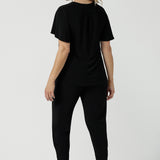 Back view of a size 10 woman wears the Lila Top in Black, a jersey workwear top for women for flutter sleeve and v-neckline. Made in Australia for women size 8-24.