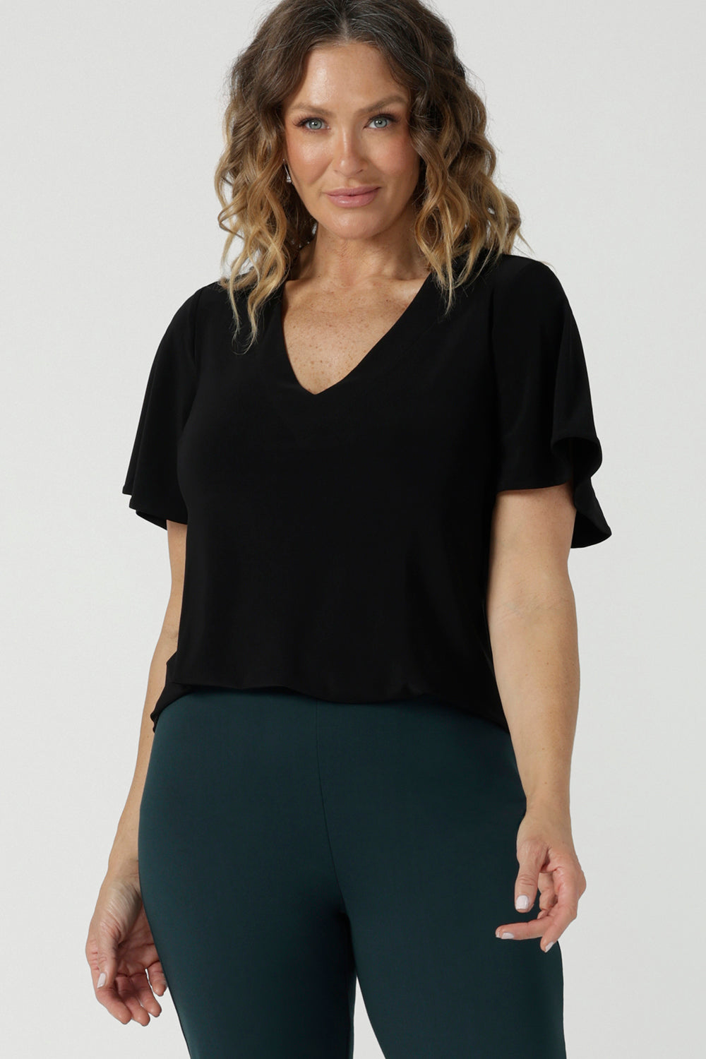 A size 10 woman wears the Lila Top in Black, a jersey workwear top for women for flutter sleeve and v-neckline. Made in Australia for women size 8-24.