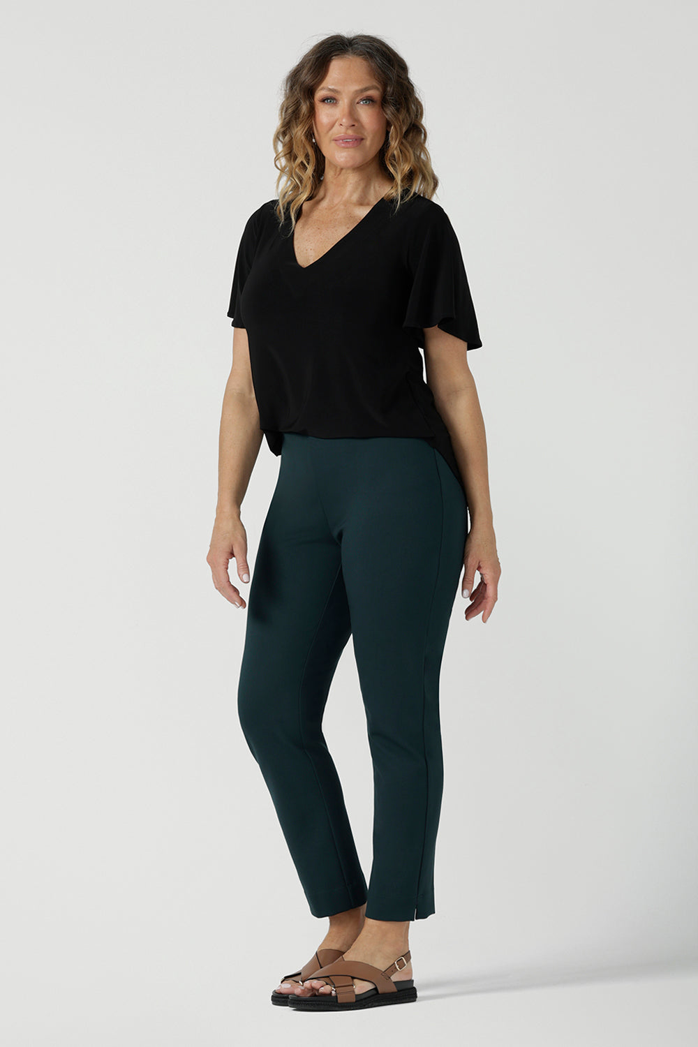 Back view of a size 10 woman wears the Lila Top in Black, a jersey workwear top for women for flutter sleeve and v-neckline. Made in Australia for women size 8-24. Styled back with a Paxton Pant in Alpine. 