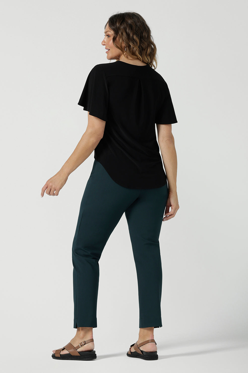 Back view of a size 10 woman wears the Lila Top in Black, a jersey workwear top for women for flutter sleeve and v-neckline. Made in Australia for women size 8-24. Styled back with a Paxton Pant in Alpine.