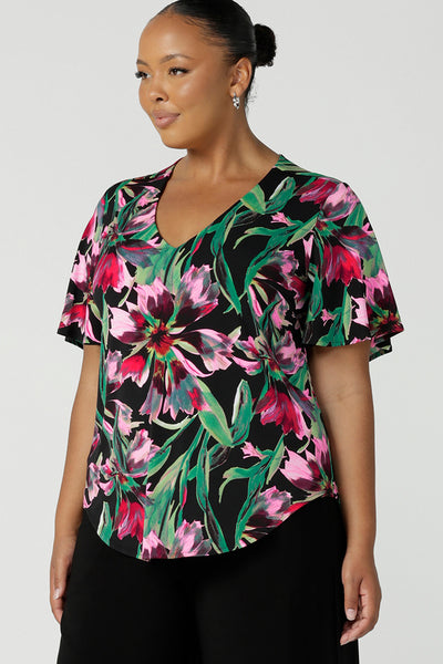 A plus size, size 18 woman wears a floral print jersey, V-neck top with flutter sleeves. A good top for summer casual wear, or style tucked as a workwear top. Shop made in Australia tops in petite to plus sizes online at Australian fashion brand, Leina & Fleur.