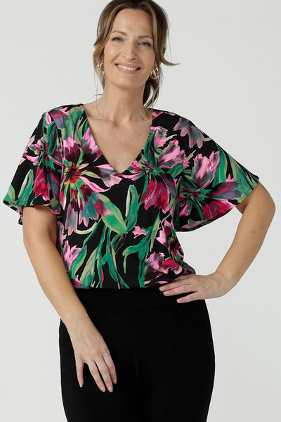 A size 10, 40 plus woman wears a floral print jersey, V-neck top with flutter sleeves. A good top for summer casual wear, or style tucked as a workwear top. Shop made in Australia tops in petite to plus sizes online at Australian fashion brand, Leina & Fleur.