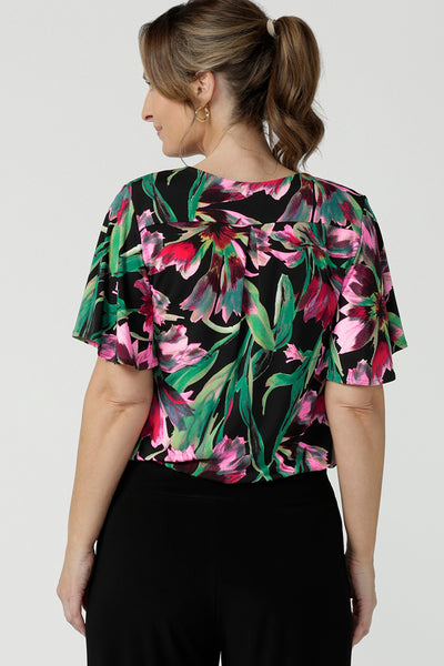 Back view of a size 10, 40 plus woman wearing a floral print jersey, V-neck top with flutter sleeves. A good top for summer casual wear, or style tucked as a workwear top. Shop made in Australia tops in petite to plus sizes online at Australian fashion brand, Leina & Fleur.