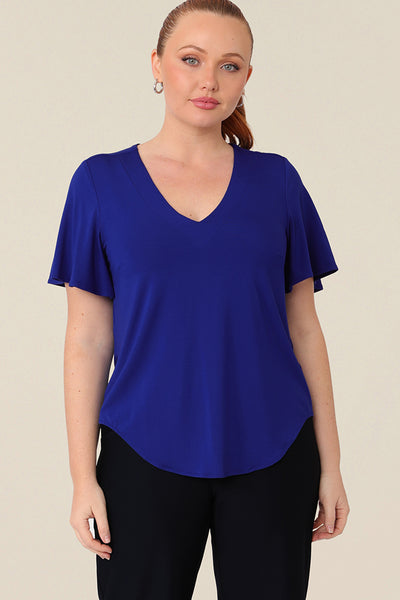 A size 12 curvy woman wears a blue bamboo jersey top with a V-neck and short flutter sleeves. It is a lightweight and breathable top thanks to its natural and sustainable bamboo fibres, and being made in Australia, it is part of L&Fs move towards greater sustainability and eco-conscious fashion.