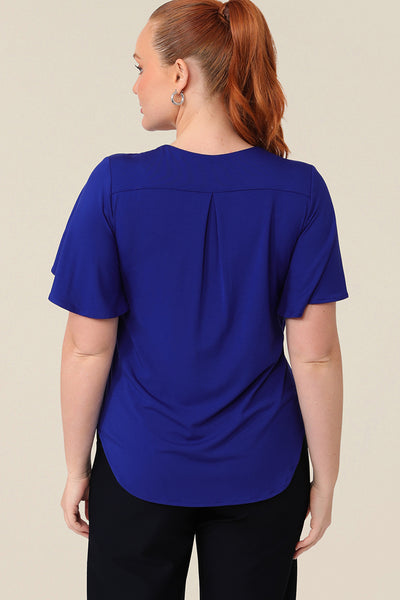 Back view of a size 12 curvy woman wearing a blue bamboo jersey top with a V-neck and short flutter sleeves. It is a lightweight and breathable top thanks to its natural and sustainable bamboo fibres, and being made in Australia, it is part of L&Fs move towards greater sustainability and eco-conscious fashion.