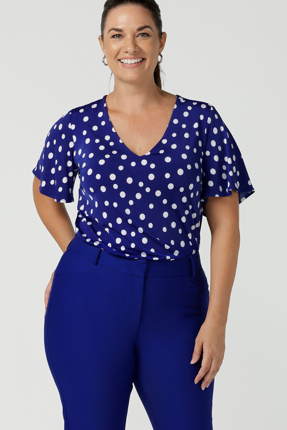 Close up of the Lila top in Cobalt Spot on a happy size 12 woman. Curved hemline and flutter sleeves. A abstract polka dot print. Made in Australia for women size 8 to 24. 