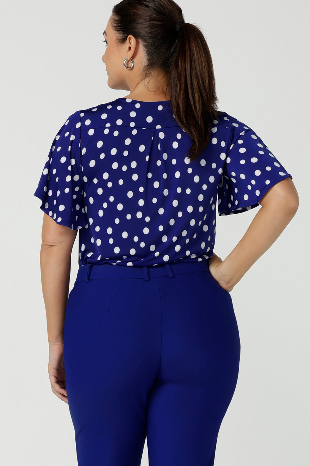 Back view of the Lila top in Cobalt Spot on a happy size 12 woman. Curved hemline and flutter sleeves. A abstract polka dot print. Made in Australia for women size 8 to 24.