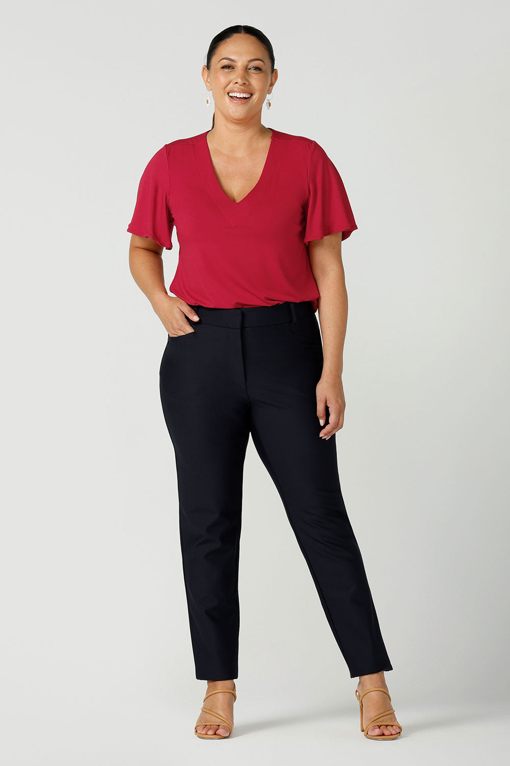 A size 12 woman wears Lulu cigarette pants in navy ponte with a matching jacket. A comfortable tailored work pant with fly front and belt loops. Styled back with a Lila top in red bamboo. A great office look for the festive season. Made in Australia for women sizes 8 - 24.