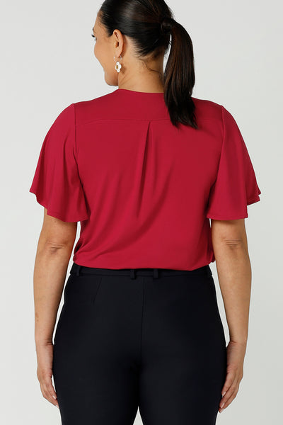 Back view of a size 12 curvy woman wears the Lila Top in Flame bamboo in a Christmas red colour. The bamboo material is breathable, soft and temperature regulating. The Lila top features a flutter sleeve and deep v-neckline. Made in Australia for women size 8-24.