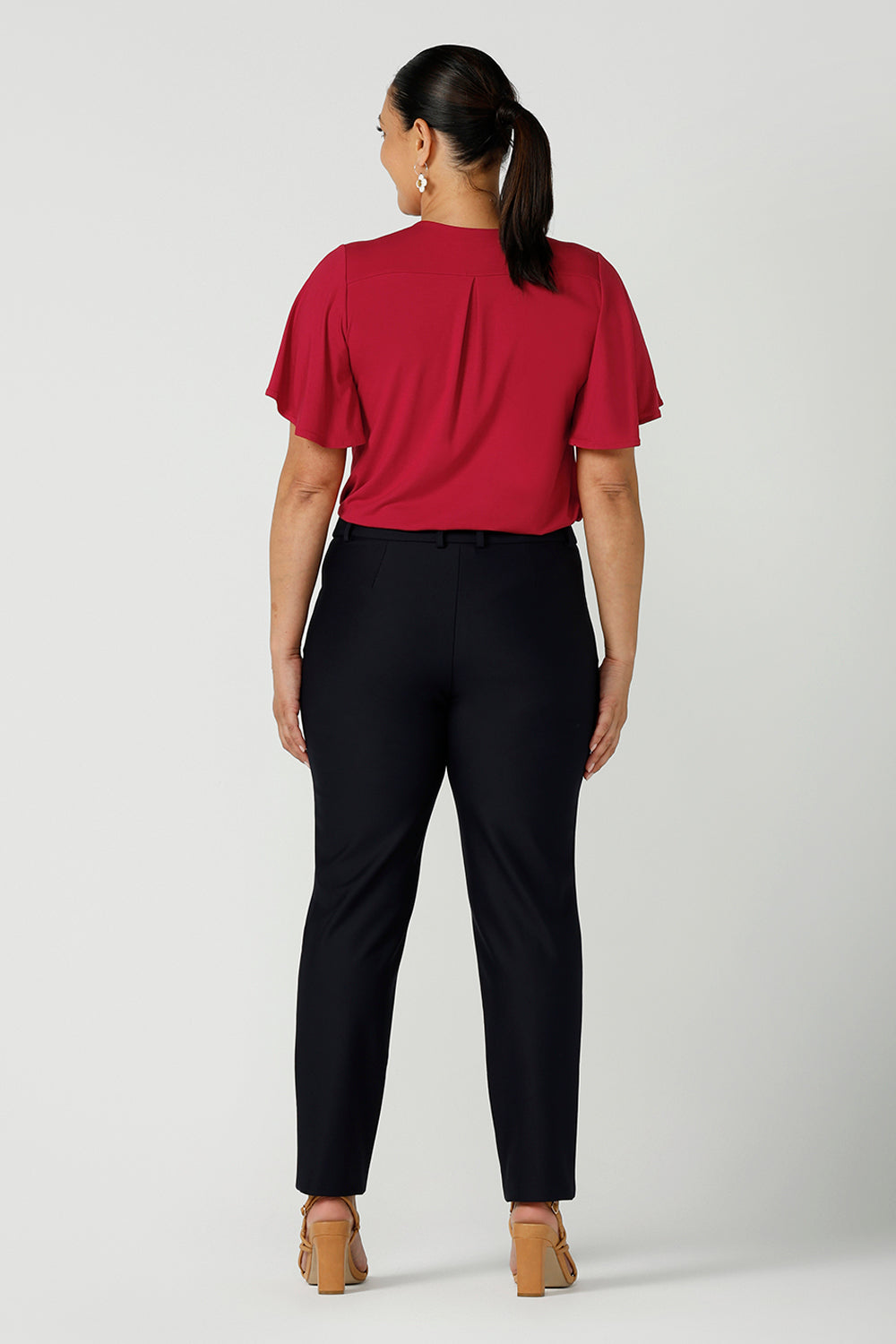 Back view of a size 12 woman wears Lulu cigarette pants in navy ponte with a matching jacket. A comfortable tailored work pant with fly front and belt loops. Styled back with a Lila top in red bamboo. A great office look for the festive season. Made in Australia for women sizes 8 - 24.
