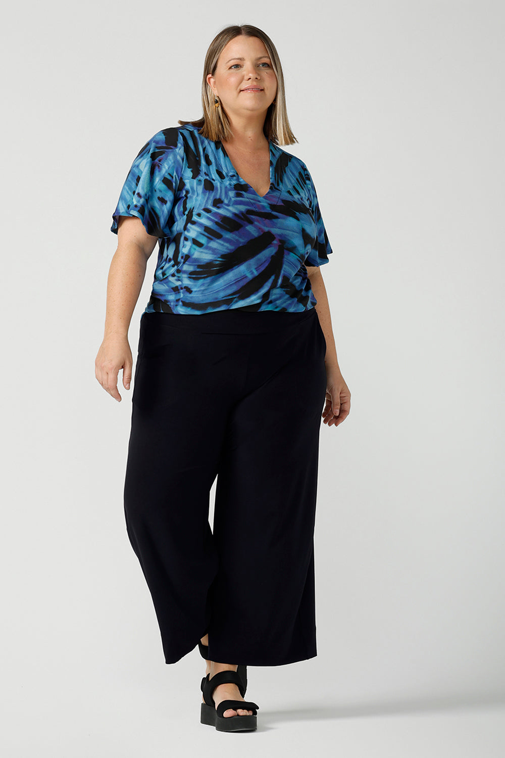 Curvy size 18 woman wears an Lila printed top in Flutter print. Digitally printed with cobalt, purple and black on a butterfly wing abstract print. Made in Australia for women 8 - 24. Styled back with navy jersey culottes.