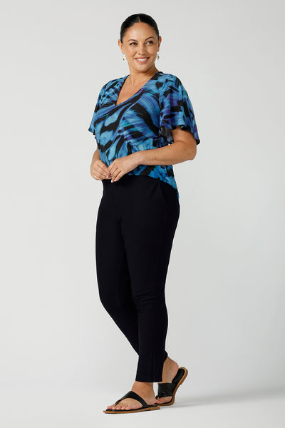 Curvy size 18 woman wears an Lila printed top in Flutter print. Digitally printed with cobalt, purple and black on a butterfly wing abstract print. Made in Australia for women 8 - 24. Styled back with navy slim fit brooklyn pants.