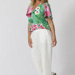 Over 40 year old woman wears wrinkle-resistant V neck top. High quality ensures you look polished all day, with minimal effort—ideal for busy, on-the-go events. Made in Australia, it combines quality craftsmanship with easy-care convenience, making it a go-to piece for any summer occasion. Whether you're attending a garden party, a casual gathering, or a more formal event, this top effortlessly elevates your style.