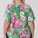 Back view of floral top, featuring shirt tail hemline and flutter sleeves. The Malibu print is on a teal-blue slinky jersey base with print details in shades of green, pink, white, yellow and brown. The fabric has a soft stretch and cooling effect. Sizes 8-24 are now available to shop.