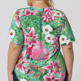 Back view of floral top, featuring shirt tail hemline and flutter sleeves. The Malibu print is on a teal-blue slinky jersey base with print details in shades of green, pink, white, yellow and brown. The fabric has a soft stretch and cooling effect. Sizes 8-24 are now available to shop.