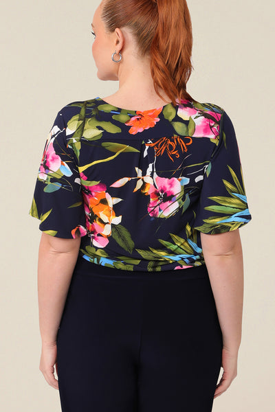 Back view of A size 12 curvy woman wears a floral jersey top with a V-neck and short flutter sleeves. It is a lightweight and crease-free top thanks to its stretch jersey fabric. Made in Australia, for sizes 8-24.