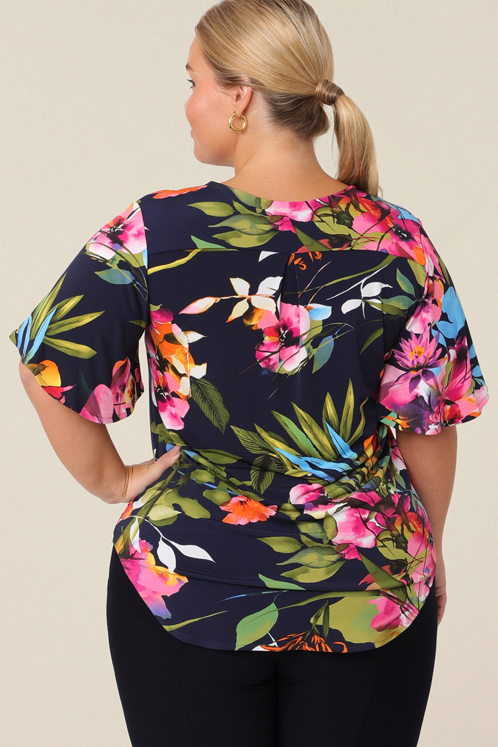 Back view of a plus size, size 14 woman wears a V-neck floral top with short flutter sleeves. Made from dry-touch jersey, this top is comfortable for everyday style. Designed and made in Australia for petite to plus size women.