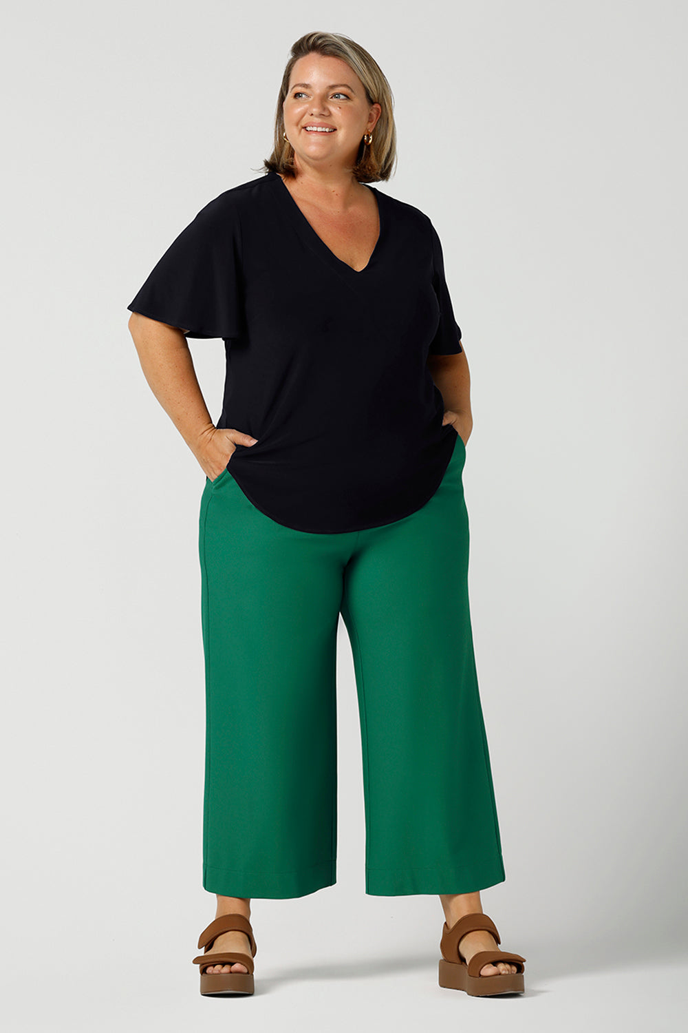 Worn by a size 18, plus size woman, this is a semi-fitted, V-neck top with flutter sleeves in navy blue jersey. Made in Australia by women's clothing brand, Leina & Fleur , this classic navy top is worn with wide leg emerald green tailored pants for summer. Great for capsule wardrobes, smart casual wear and as a work blouse, shop this top and other Australian-made women's clothing online in sizes 8 to 24 at Leina & Fleur's online fashion boutique!