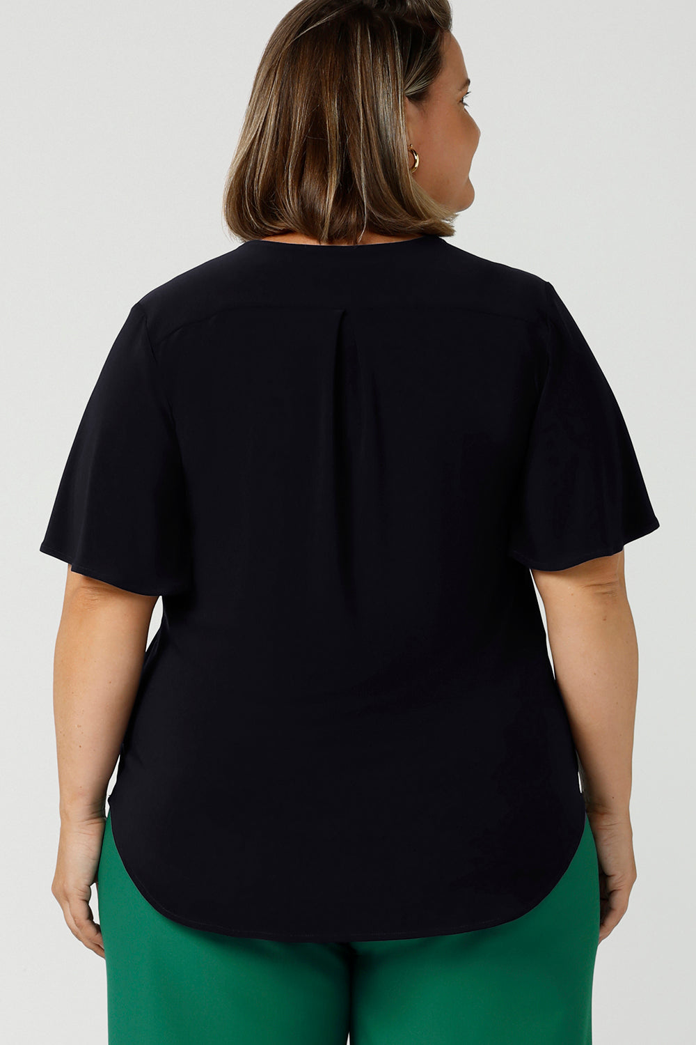 Back view of a semi-fitted, V-neck top with flutter sleeves in navy blue jersey. Made in Australia by women's clothing brand, Leina & Fleur , this plus size navy top is worn by a size 18, curvy woman. Great for capsule wardrobes, smart casual wear and as a work blouse, shop this top and other Australian-made women's clothing online in sizes 8 to 24 at Leina & Fleur's online fashion boutique!