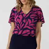 A size 10 woman wears the Lila Top in Pink Jungle. A flutter sleeve v-neck top made in Jersey fabric. Easy care work tops for women. Petite to plus size and size inclusive 8-24.