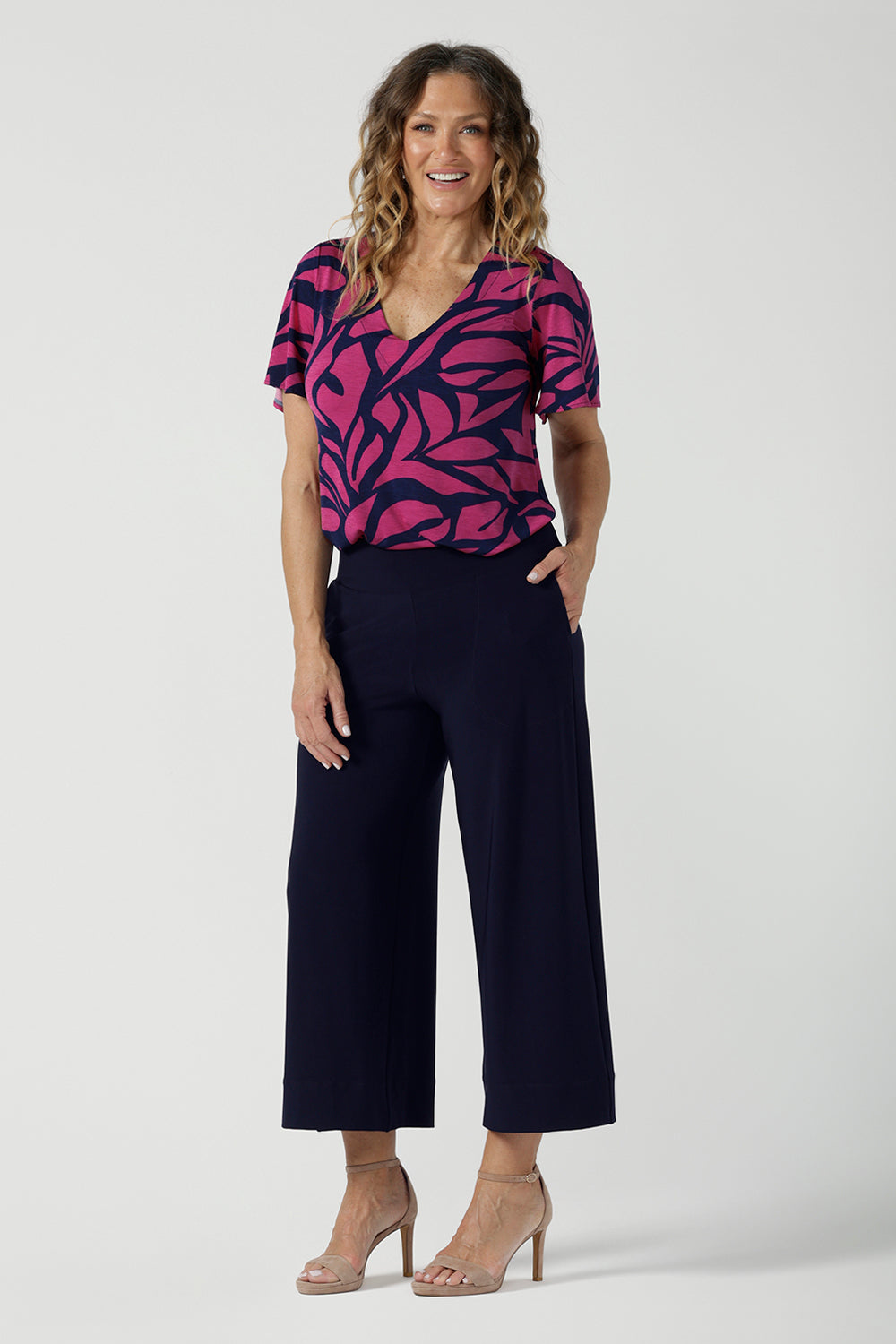 A size 10 woman wears the Lila Top in Pink Jungle. A flutter sleeve v-neck top made in Jersey fabric. Easy care work tops for women. Petite to plus size and size inclusive 8-24.