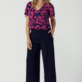 A size 10 woman wears the Lila Top in Pink Jungle. A flutter sleeve v-neck top made in Jersey fabric. Easy care work tops for women. Petite to plus size and size inclusive 8-24.