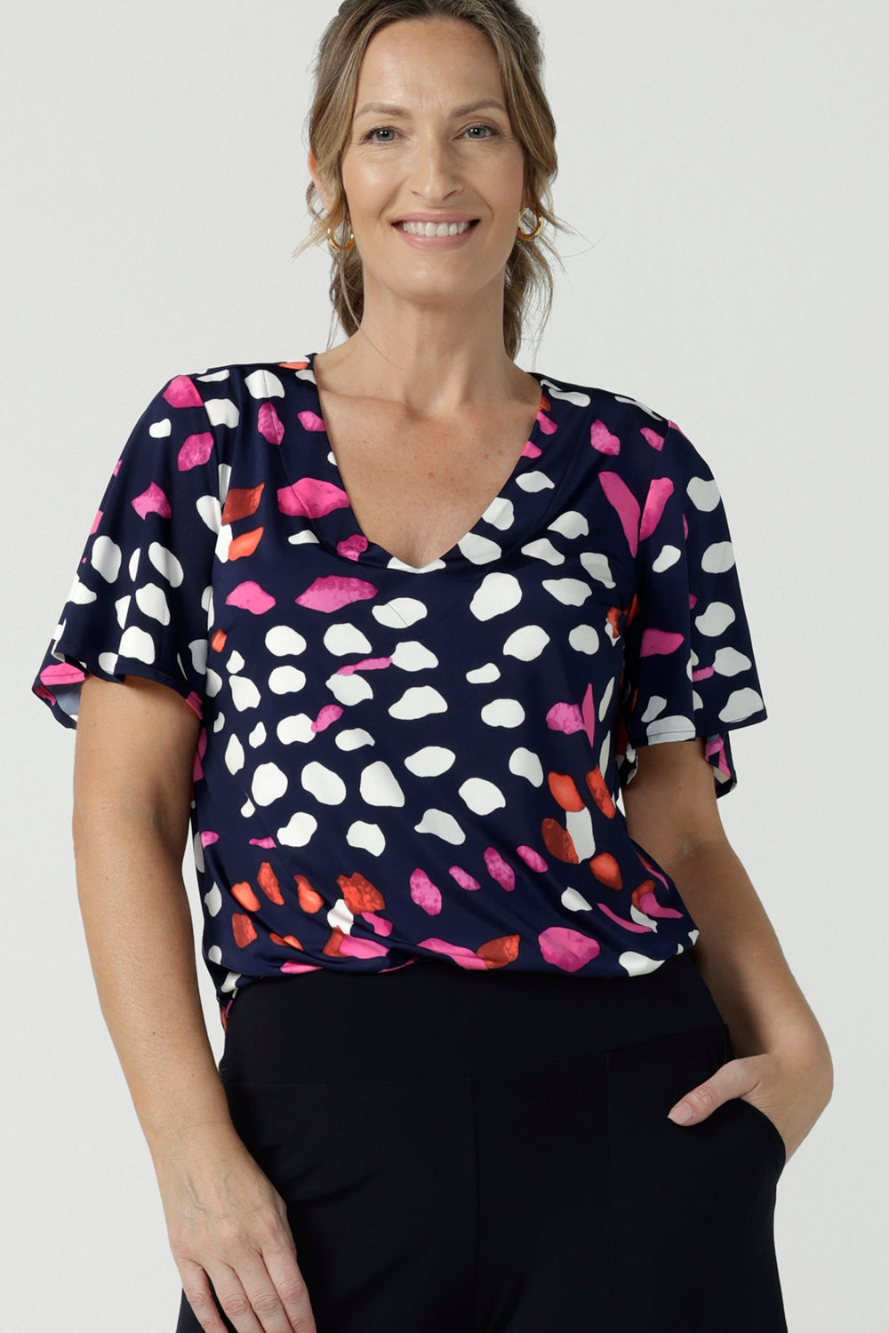 A size 10, 40 plus woman wears an abstract print jersey, V-neck top with flutter sleeves. A good top for summer casual wear, or style tucked as a workwear top. Shop made in Australia tops in petite to plus sizes online at Australian fashion brand, Leina & Fleur.