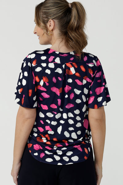 Back view of a size 10, 40 plus woman wearing an abstract print jersey, V-neck top with flutter sleeves. A good top for summer casual wear, or style tucked as a workwear top. Shop made in Australia tops in petite to plus sizes online at Australian fashion brand, Leina & Fleur.