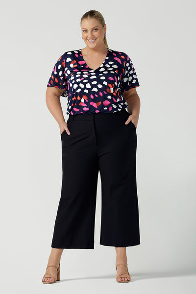 A plus size, size 18 woman wears a abstract print jersey, V-neck top with flutter sleeves. A good top for summer casual wear, or style tucked as a workwear top. Shop made in Australia tops in petite to plus sizes online at Australian fashion brand, Leina & Fleur.