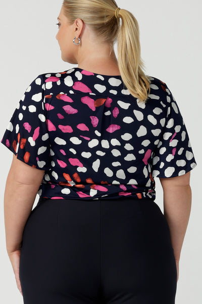 Back view of a plus size, size 18 woman wearing a abstract print jersey, V-neck top with flutter sleeves. A good top for summer casual wear, or style tucked as a workwear top. Shop made in Australia tops in petite to plus sizes online at Australian fashion brand, Leina & Fleur.