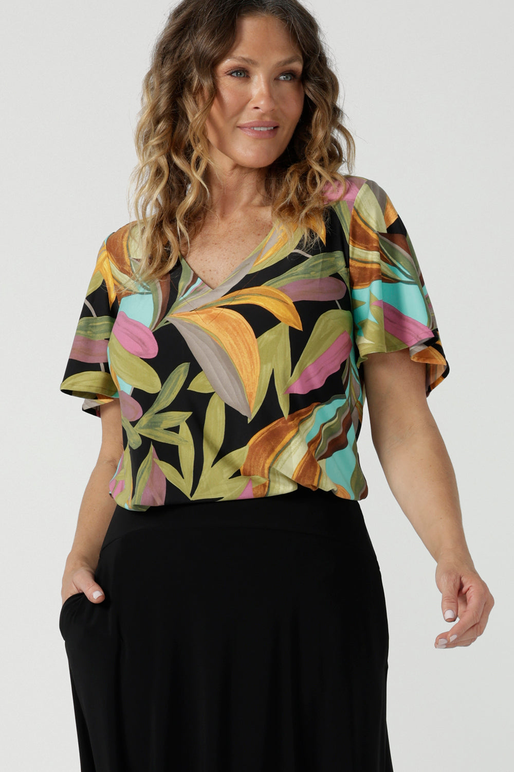 A size 10 woman wears the Lila top in women with a flutter sleeve and a v-neckline. Jersey top for women, comfortable workwear and made in Australia for women. Size 8-24. 