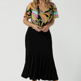 A size 10 woman wears the Lila top in women with a flutter sleeve and a v-neckline. Jersey top for women, comfortable workwear and made in Australia for women. Size 8-24. Styled back with a Berit Maxi Skirt.