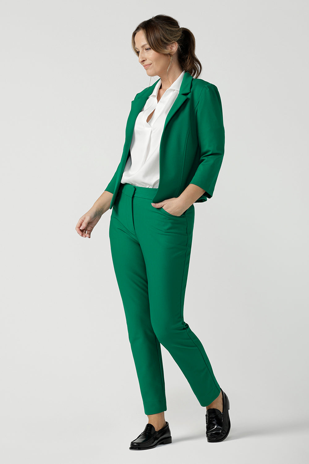 A size 10 woman wears a tailored jacket with open front and collar and notch lapels is made in Emerald green ponte fabric. Styled with Emerald green tailored pants, and a white collared shirt for a fresh workwear look. Shop exclusive luxury, this work jacket is available at Australian and New Zealand women's clothing label, L&F.