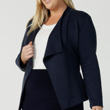 A size 18 woman wears the Lyndon Jacket in Bluestone. A wrap style jacket with waist belt and collared neckline. Made in soft luxurios modal. Rug up on the way to the office or weekend winter get away. Made in Australia for women size 8 -24.